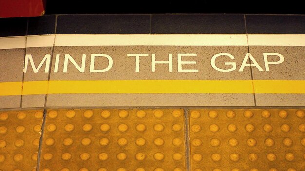 Photo mind the gap sign on the subway train platform floor and yellow color and dirty and no people.