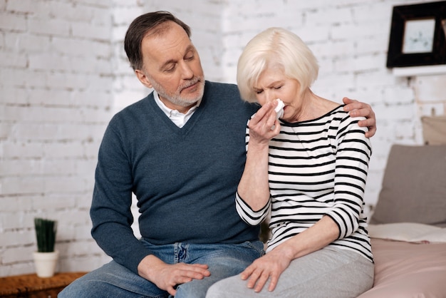 Do not mind. Senior nice woman is crying near her aged husband trying give her solace.