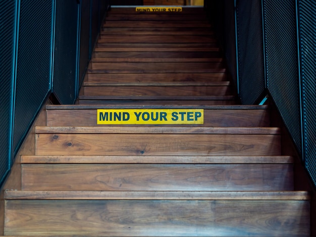 Mind your step black text on yellow warning sign on wooden\
staircase