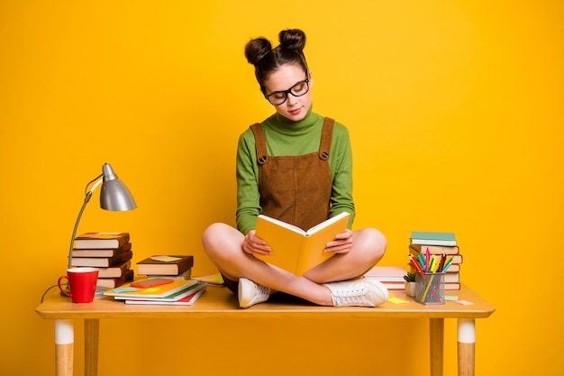 Minded girl sit table read book  on yellow background