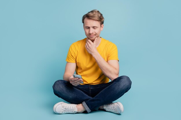 Minded thoughtful guy sit floor hold telephone read post think wear casual clothes isolated on turquoise background