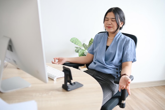 Mindful peaceful young businesswoman practicing breathing yoga exercises at workplace