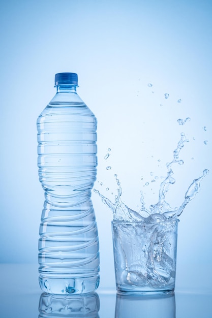 Mineral water bottle and water glass with spash on blue background with copy space Vertical format