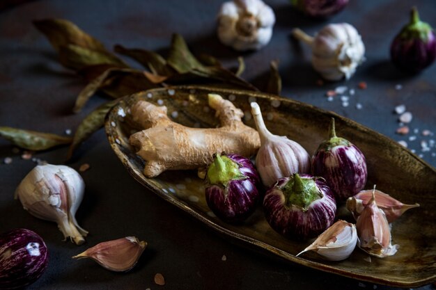 Mini aubergines, gember, knoflook in handgemaakt keramisch bord, kristallijn roze zout op beton