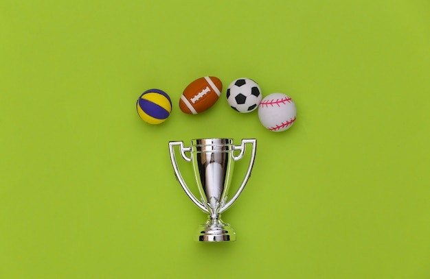 Foto mini palline di diversi sport e coppa del campione su sfondo verde. concetto di sport minimalista. vista dall'alto. disposizione piatta.