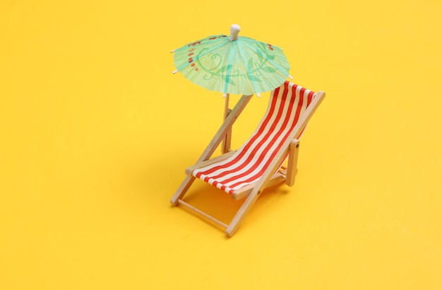 Mini beach deck chair with umbrella on yellow background Beach vacation summer time sunbathing concept