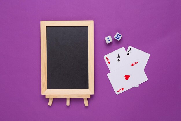 Mini blank chalk board with copy space and playing cards on purple background Gambling concept