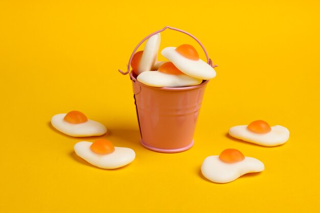 Mini bucket with marmalade fried eggs on yellow background. Sweets, pastel color trend, food concept.