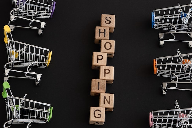 Mini color supermarket trolleys and word shopping on black background Shopping concept