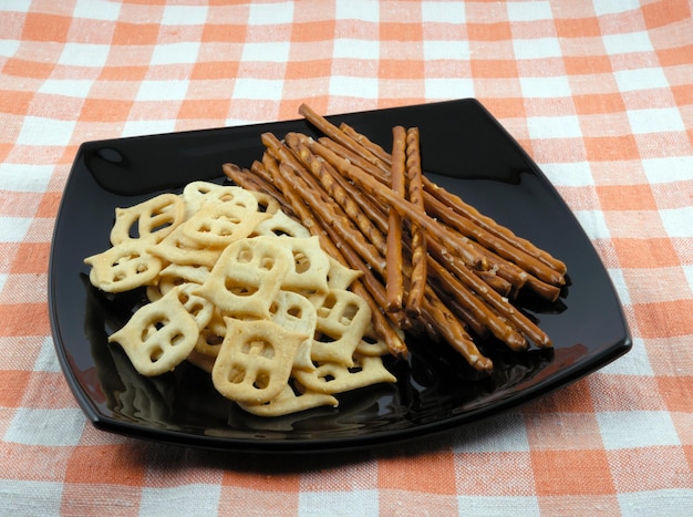 Mini crackers and salty grain sticks to beer on a black plate