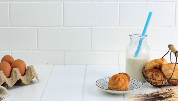 Mini-croissant met melk, schilfers gebak met boter uit het Frans. Geserveerd op plaat en geweven draadmand op witte keuken. Ruimte voor tekst kopiëren.