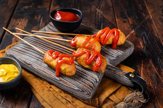 Mini Deep fried corn dogs with mustard and ketchup on wooden board Wooden background Top view