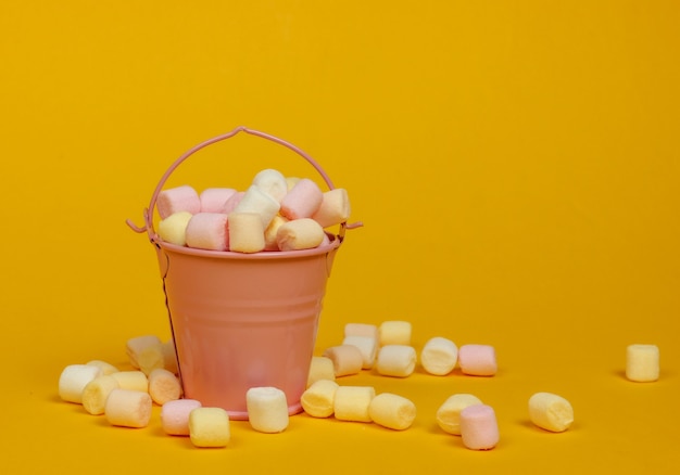 Mini-emmer met veel marshmallows op gele achtergrond. Minimalisme. Snoepgoed