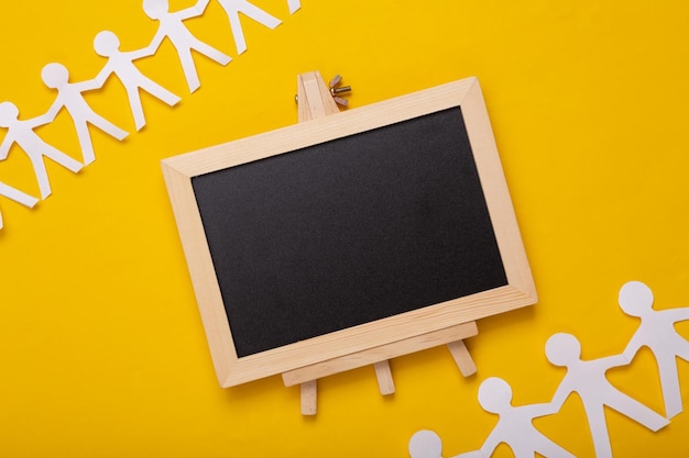 Mini Empty chalk board with copy space and papercut chain of people on yellow background Education concept