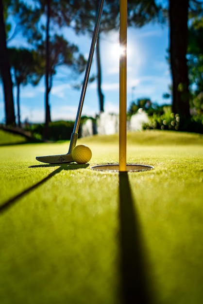 Фото Желтый мяч для мини-гольфа с битой возле лунки на закате