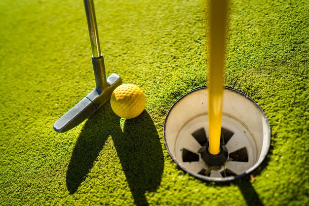 Желтый мяч для мини-гольфа с битой возле лунки на закате
