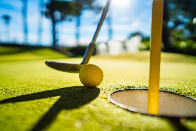 Mini Golf yellow ball with a bat near the hole at sunset