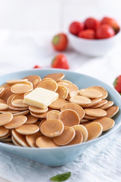 Mini granen pannenkoeken in blauwe kom met boter, aardbeien op wit