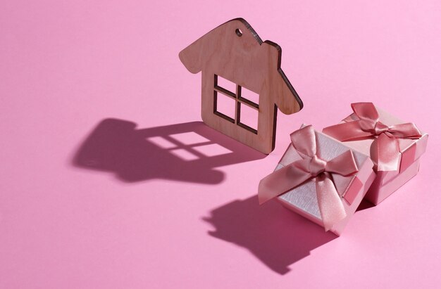 Photo mini house figure and gift box on pink pastel background. studio shot with shadow