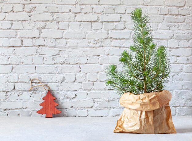 Mini-kerstboom in een ambachtelijke papieren zak op de achtergrond van de bakstenen muur, concept zonder afval