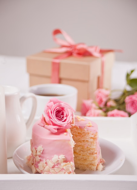 Mini-kleine cake met roze glazuur, mooie rozen, kopje koffie, geschenkdoos op de witte tafel.