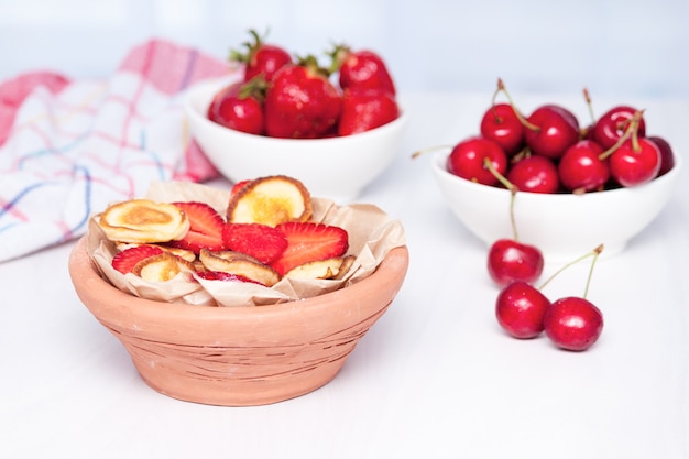 Mini kleine pannenkoeken met aardbeien en kersen op witte houten achtergrond. Trendy voedselconcept.