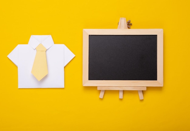 Mini leeg krijtbord met kopieerruimte en papieren overhemd met stropdas op gele achtergrond Bedrijfstrainingsconcept