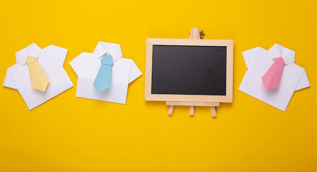 Mini leeg krijtbord met kopieerruimte en papieren overhemden met stropdassen op gele achtergrond Bedrijfstrainingsconcept