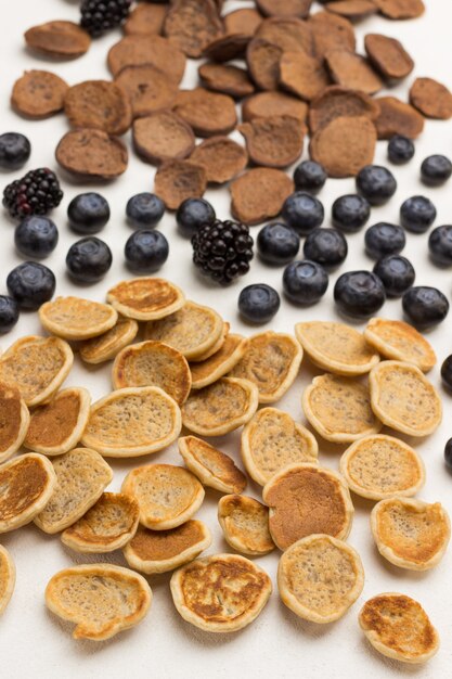 Mini pancakes and berries on white surface. Flat lay.