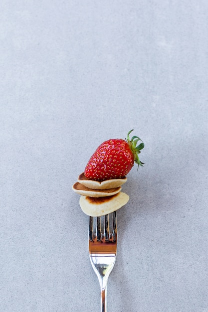 Foto mini pancake sulla forcella con fragole su uno sfondo di cemento
