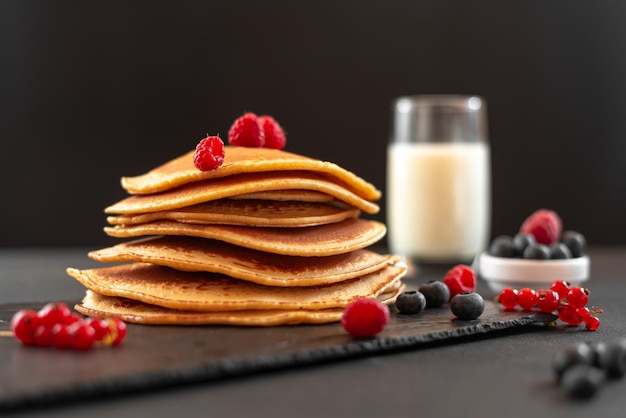 Mini pancakes with blueberries and raspberries American breakfast on a dark background