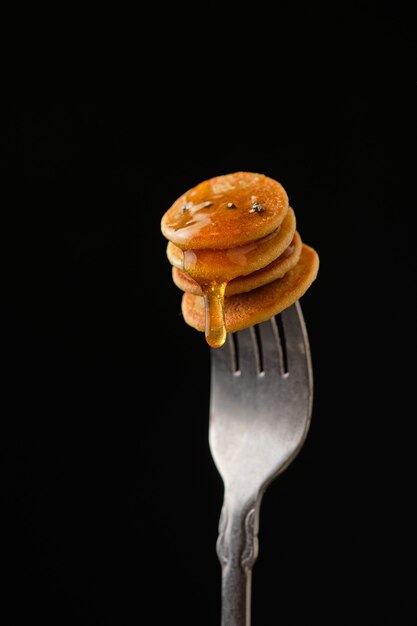 Mini pancake con miele su una forchetta su sfondo scuro