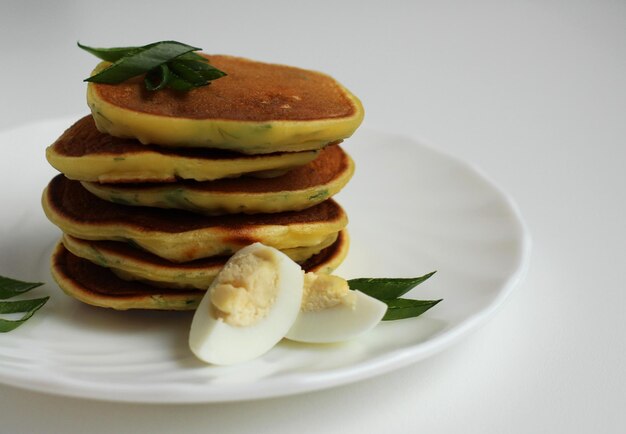 Mini pancakes with quail egg and green onions on a white plate