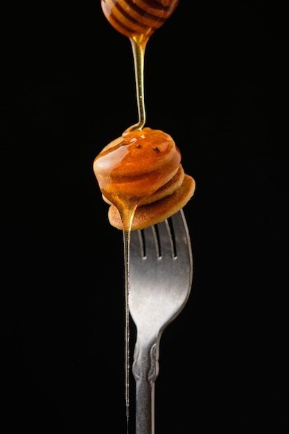 Mini pannenkoeken met honing op een vork op een donkere achtergrond