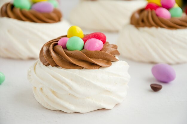 Mini Pavlova Birds Nest with chocolate cream and colored candy. Merengue Cookies. Food idea for kids. Easter cake. Horizontal orientation. Close up.