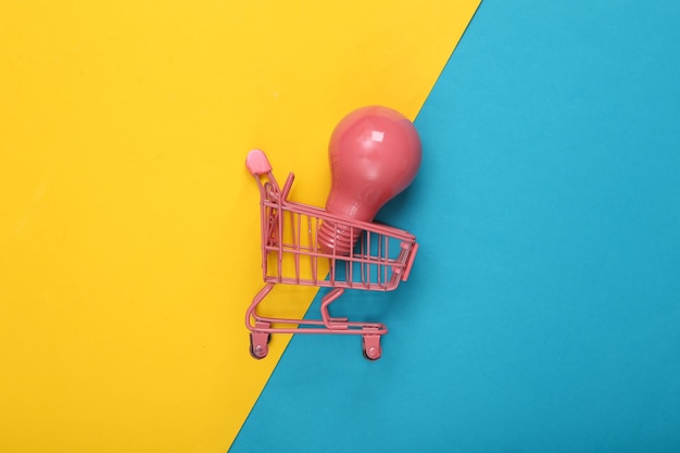 Mini pink supermarket trolley with light bulb on a blueyellow background Fresh idea Creative layout Top view Flat lay