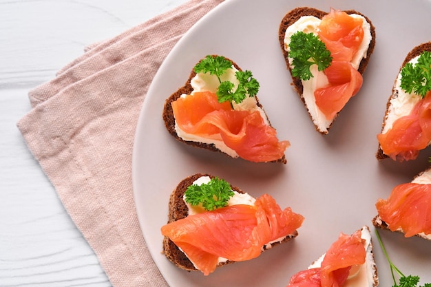 Mini sandwiches met zalm, kwark, peterselie en roggebrood in hartvorm. Valentijnsdag zelfgemaakte creatieve gerechten. Houd van ontbijtontwerp. Selectieve focus en kopieerruimte