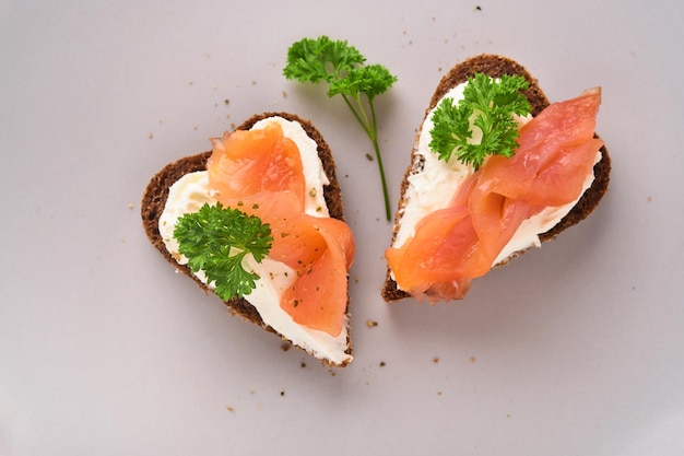 Mini sandwiches met zalm, kwark, peterselie en roggebrood in hartvorm. Valentijnsdag zelfgemaakte creatieve gerechten. Houd van ontbijtontwerp. Selectieve focus en kopieerruimte