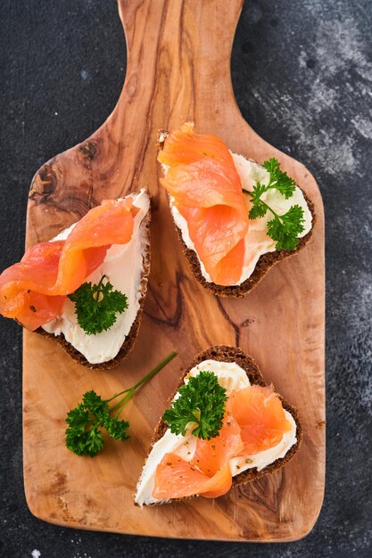 Mini sandwiches with salmon, curd cheese, parsley and rye bread in form of hearts. Valentine's day homemade creative food. Love breakfast design. Selective focus and copy space