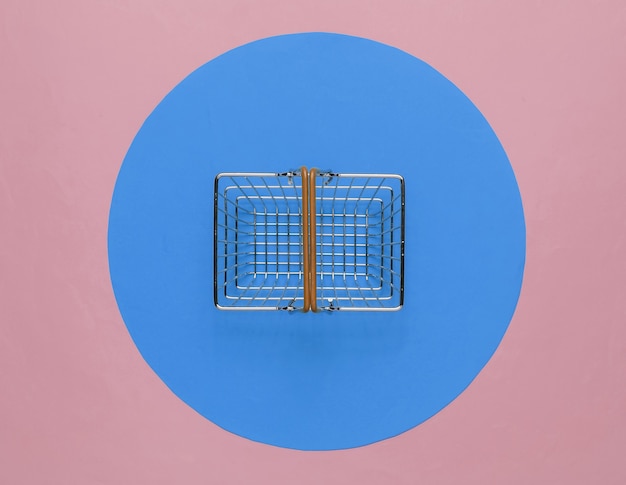 Mini shopping basket on pink background with blue circle. Top view