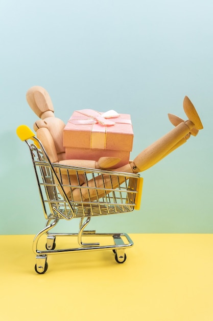 Mini shopping cart buying gifts with wooden mannequin advertisement for gift from all or composition concept Vertical photo