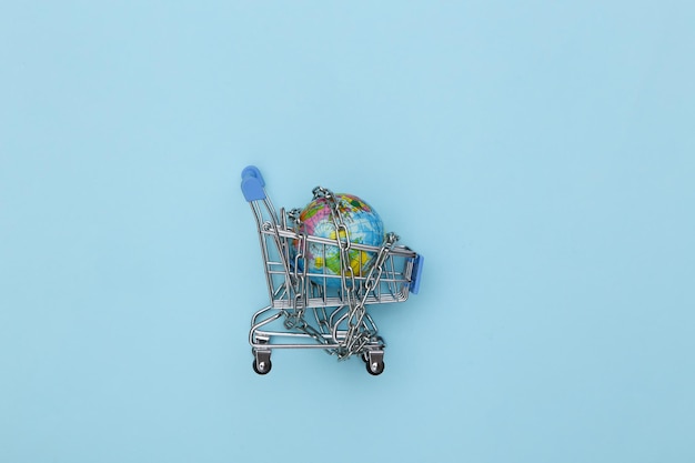 Mini shopping cart and globe wrapped in a steel chain on blue background. Top view