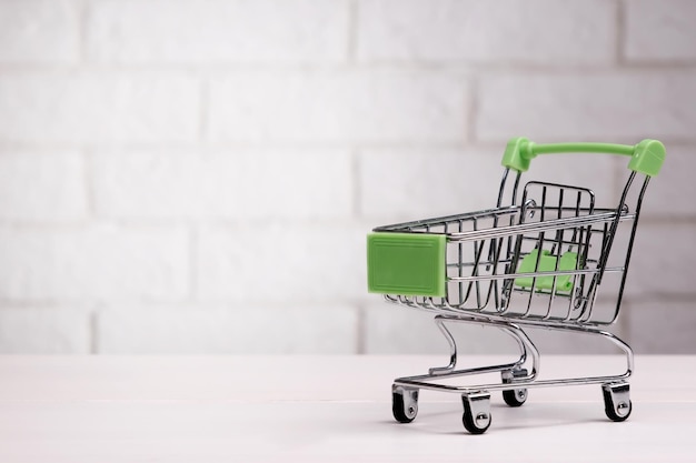 Mini shopping cart on table against brick wall background