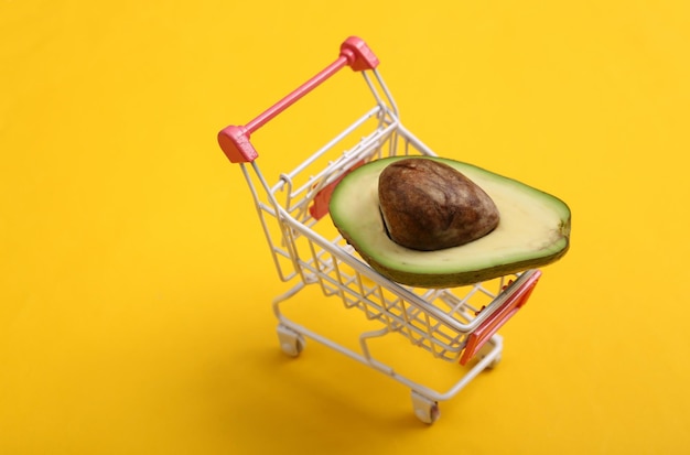 Mini shopping cart with half avocado on yellow background