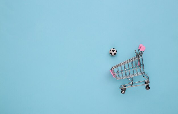 Mini shopping cart with a soccer ball on a blue background. Top view