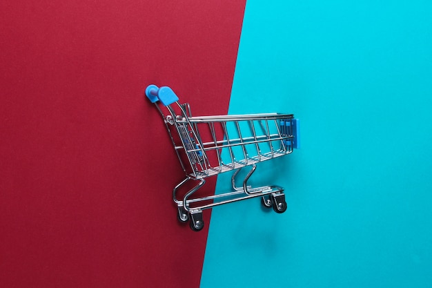 Mini shopping trolley on a red-blue table. Top view, minimalism