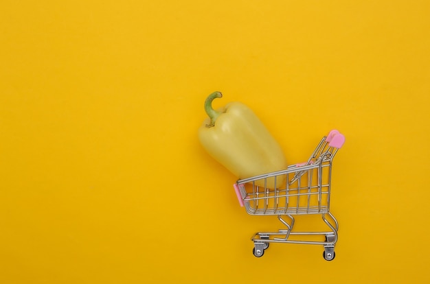 Mini shopping trolley with Bell pepper on yellow background. Top view