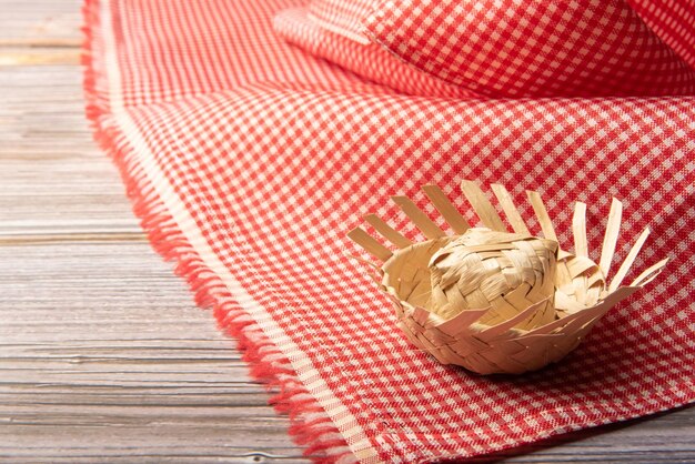 Mini straw hat used in Junina party decoration in Brazil placed on red and white checkered tablecloth selective focus