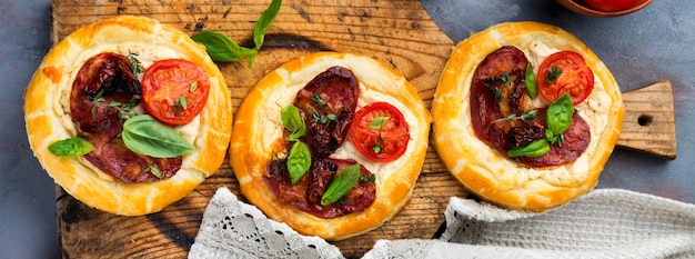 Mini tarts with dried meat, tomatoes, ricotta, thyme, basil and olives on a gray concrete background. Rustic style. Selective focus. Top view