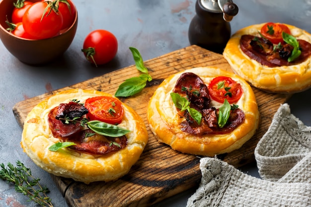 Mini tarts with dried meat, tomatoes, ricotta, thyme, basil and olives on a gray concrete. Rustic style